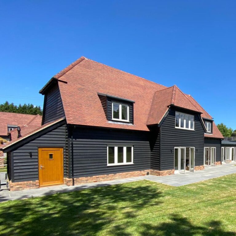 Close-up of completed timber frame homes with black weatherboarding and dormer roof windows.